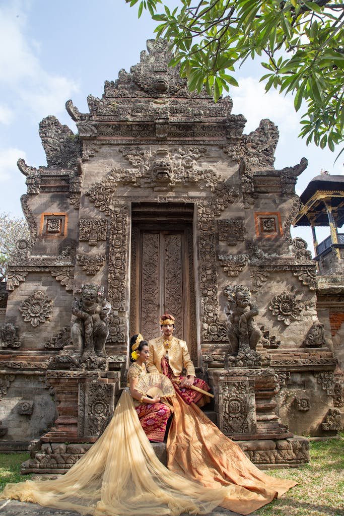A couple in traditional Balinese attire in front of a historic temple in Bali, Indonesia.