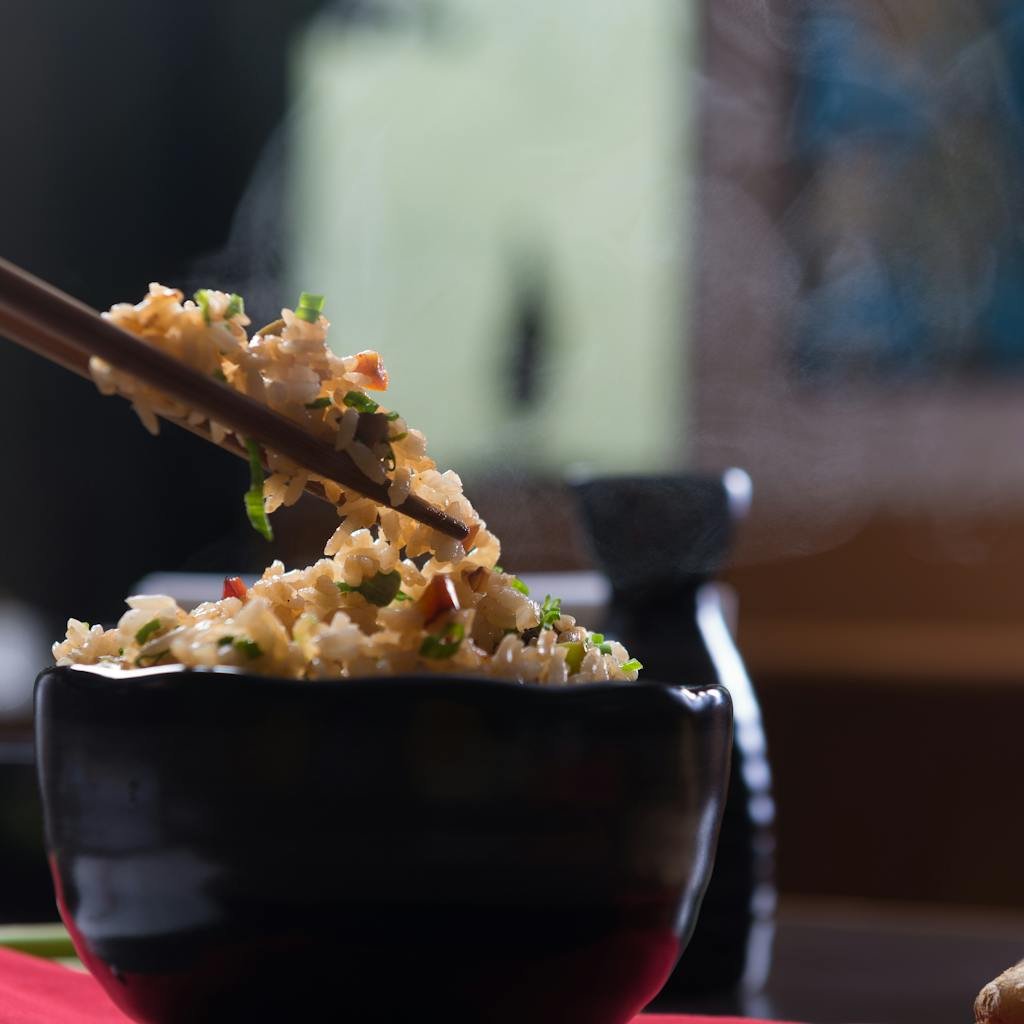 Delicious steaming fried rice in a black ceramic bowl with chopsticks, perfect for an appetizing meal.