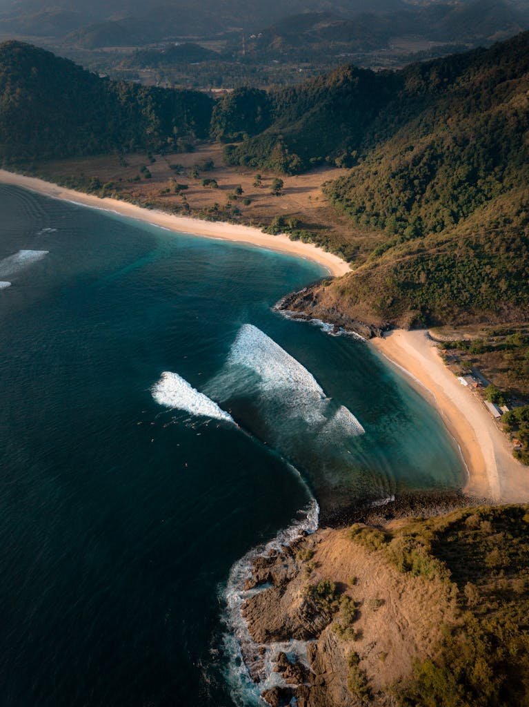 Stunning aerial view of a serene beach and lush hills in Lombok, Indonesia.